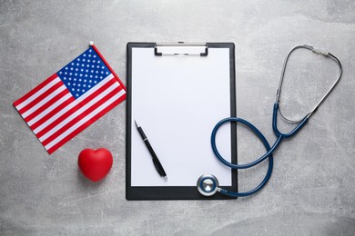 Photo of American flag, heart, clipboard and stethoscope on light grey table, flat lay