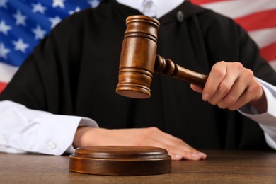 Judge with gavel at wooden table against flag of United States, closeup