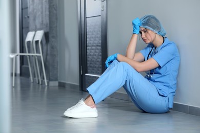 Photo of Exhausted doctor sitting on floor in hospital, space for text