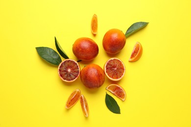 Many ripe sicilian oranges and leaves on yellow background, flat lay