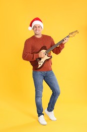 Man in Santa hat playing electric guitar on yellow background. Christmas music