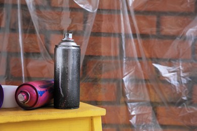 Used cans of spray paints on table near brick wall indoors, space for text. Graffiti supplies
