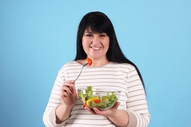 Beautiful overweight woman eating salad on light blue background. Healthy diet