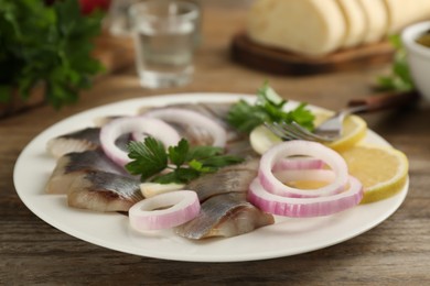 Photo of Sliced salted herring fillet served with onion rings, parsley and lemon on wooden table, closeup
