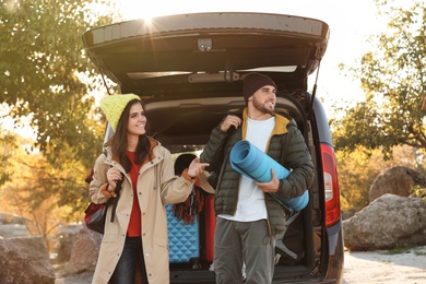 Young couple with camping equipment near car trunk outdoors