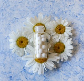 Bottle of homeopathic remedy and beautiful chamomiles on white background, top view