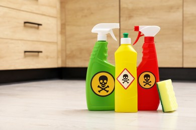Photo of Bottles of toxic household chemicals with warning signs and scouring sponge on floor indoors, space for text