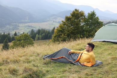 Man in sleeping bag near camping tent on hill, space for text
