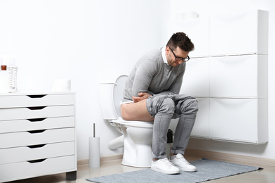 Man with stomach ache sitting on toilet bowl in bathroom