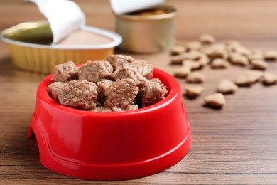 Wet pet food in feeding bowl on wooden table, closeup. Space for text