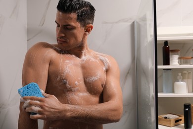 Handsome man with sponge taking shower at home