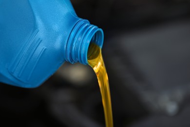 Pouring motor oil from blue container against blurred background, closeup. Space for text