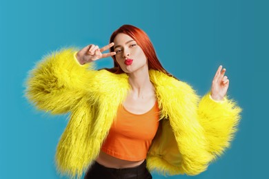 Photo of Stylish woman with red dyed hair blowing kiss on light blue background