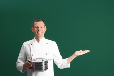 Happy male chef with cooking pot on dark green background. Space for text
