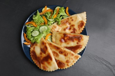 Delicious fried chebureki with vegetables served on black table, flat lay