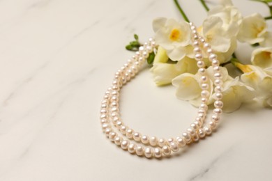 Photo of Beautiful pearl necklace and flowers on white marble table, closeup. Space for text