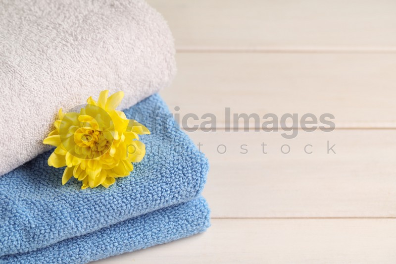 Photo of Closeup view of soft folded towels and chrysanthemum on white wooden table, space for text