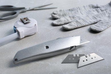 Utility knife, blades and measuring tape on light grey table, closeup