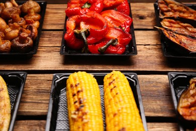 Plastic containers with different grilled meal on wooden table, closeup. Food delivery service