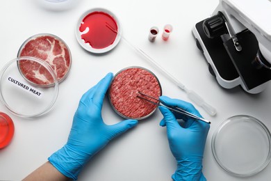 Scientist taking sample of minced cultured meat at white lab table, top view