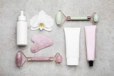 Gua sha stone, face rollers, cosmetic products and orchid flower on light table, flat lay