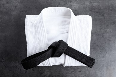 Photo of Folded white kimono and black belt on grey stone background, top view