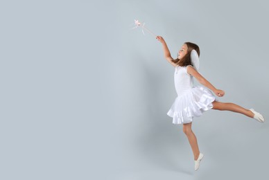 Cute little girl in fairy costume with wings and magic wand on light background. Space for text