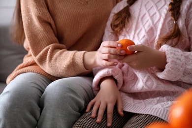 Girls with fresh tangerine sitting on sofa indoors, closeup