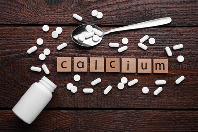 Word Calcium made of cubes with letters, spoon and pills on wooden table, top view