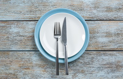 Photo of Ceramic plates, fork and knife on wooden table, top view