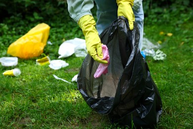 Photo of Woman with plastic bag collecting garbage on green grass outdoors, closeup