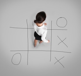 Young woman and illustration of tic-tac-toe game on grey background, above view. Business strategy concept 