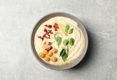 Tasty hummus with garnish in bowl on grey table, top view