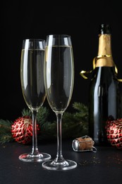 Happy New Year! Bottle of sparkling wine, glasses and festive decor on table against black background