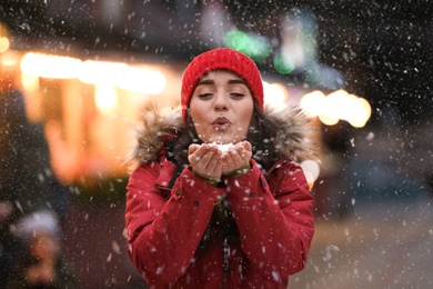 Happy young woman blowing snow at winter fair. Christmas celebration