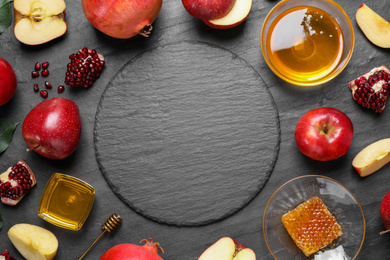 Frame of honey, apples and pomegranates on black table, flat lay with space for text. Rosh Hashanah holiday