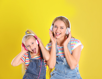 Happy mother and little daughter with headphones on yellow background