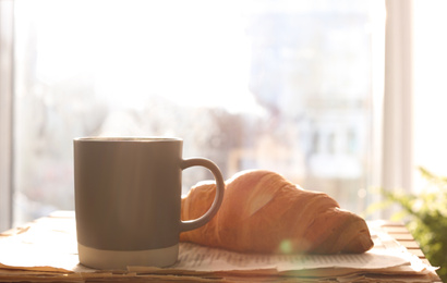Delicious morning coffee, newspaper and croissant near window indoors