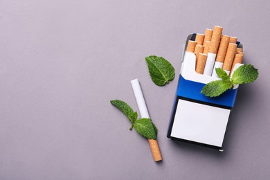 Pack of menthol cigarettes and mint leaves on grey background, flat lay. Space for text