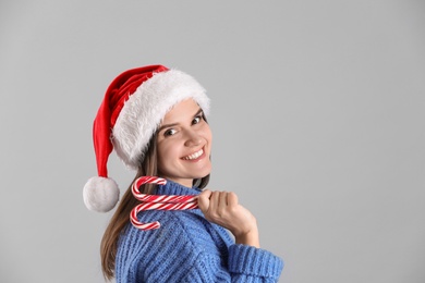 Pretty woman in Santa hat and blue sweater holding candy canes on grey background, space for text