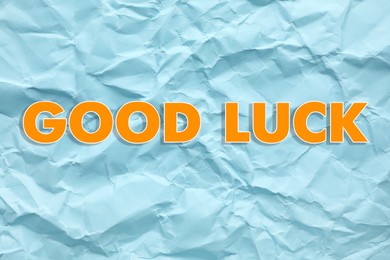 Phrase GOOD LUCK on light blue crumpled paper, top view