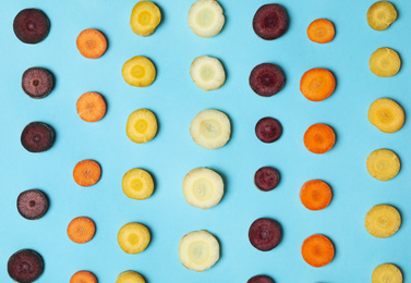 Slices of raw color carrots on light blue background, flat lay