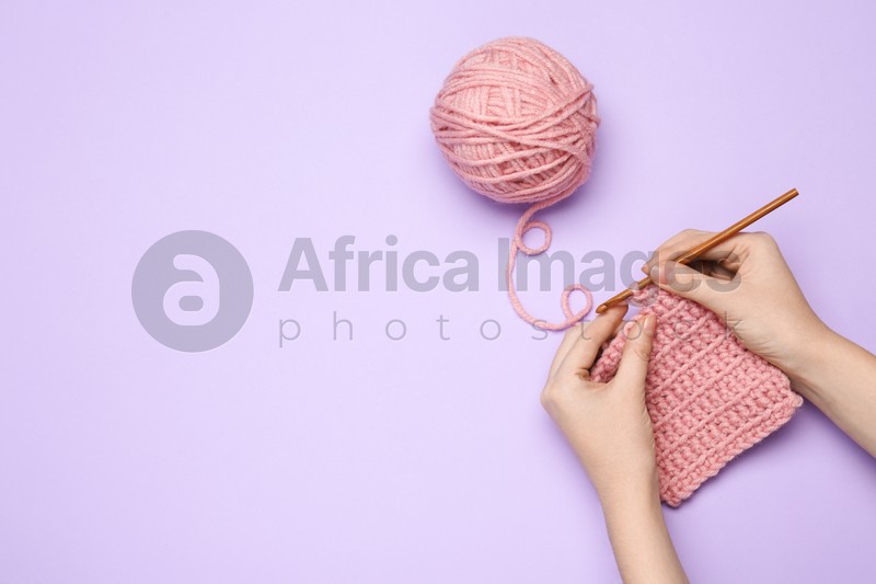 Woman crocheting with pink thread on violet background, top view. Space for text