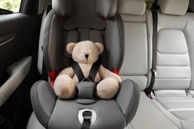 Teddy bear fastened with car safety belt in child seat