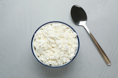 Delicious fresh cottage cheese in bowl near spoon on grey table, flat lay