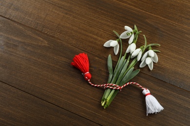 Beautiful snowdrops with traditional martisor on wooden table, flat lay and space for text. Symbol of first spring day