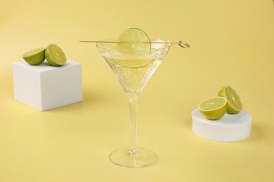 Photo of Martini cocktail with lime slice and fresh fruits on yellow background