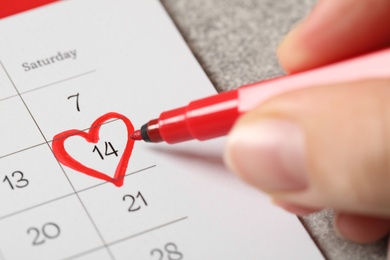 Woman marking Valentine's Day on calendar at grey table, closeup