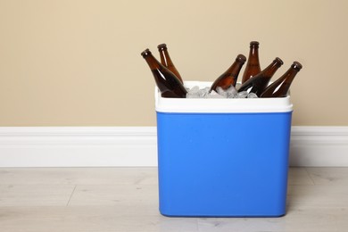 Blue plastic cool box with ice cubes and beer near beige wall indoors. Space for text