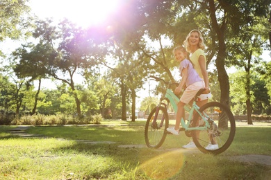 Happy mother teaching her daughter to ride bicycle in park